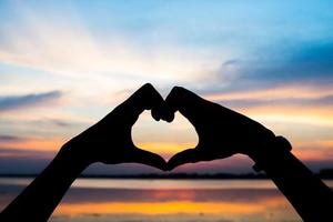 silueta de las manos de una mujer en forma de corazón con amanecer foto