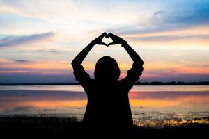 silueta de las manos de una mujer en forma de corazón con amanecer foto