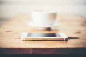 una taza de café y un teléfono inteligente en la mesa de madera en el café foto