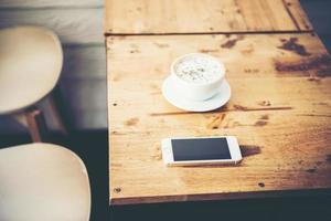 una taza de café y un teléfono inteligente en la mesa de madera en el café