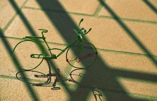 Green miniature wire bicycle with shadows on concrete pavement photo