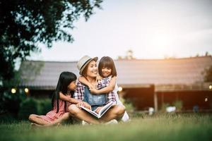 Madre contando una historia a sus dos pequeñas hijas en el jardín de la casa. foto