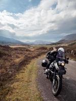 Persona en motocicleta con montañas y nublado cielo azul en Escocia foto