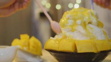 Imágenes de timelapse de personas comiendo patbingsu de cobertura de mango dulce, postre popular de hielo raspado coreano con coberturas dulces de cerca en las manos video