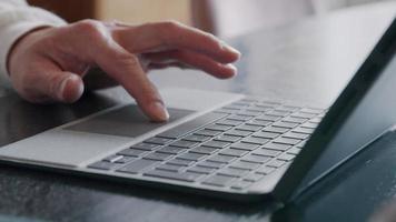 mão esquerda de um jovem asiático tocando as teclas e o mousepad do laptop video