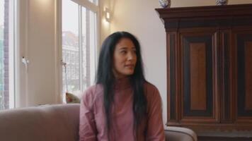 Back of mature black man, man gets up, off the sofa, leaving. Mature Asian woman sits on sofa, follows the man who leaves, with her head. Turns her head to the front, eyes down. video