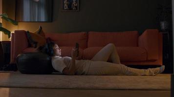 giovane donna nera sdraiata sul tappeto, cuffia sulla testa, tenendo il tablet, guardandolo video