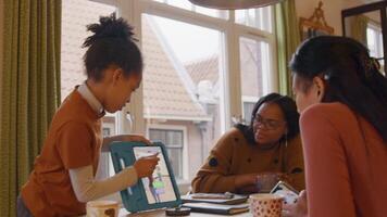 Girl standing in front of table shows tablet to two women, sitting at table video