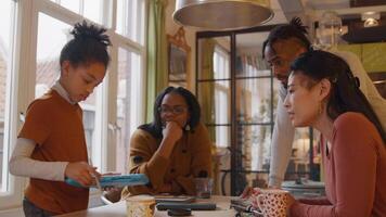 fille debout devant la table montre la tablette à deux femmes, assis à table et homme debout, appuyé sur la table video