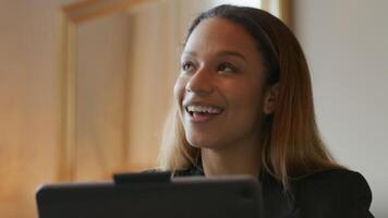 Black young woman in home office, sitting at table, having a video-call on laptop, talking spontaneously, putting her hands together, looking up, head-shoulders shot video