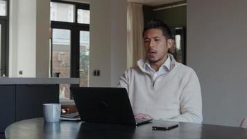 Asian young man watching laptop screen, talking, leaning back on his chair video