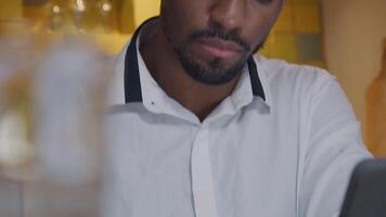 Turned face of mature black man, looks up contemplatively, turns his head, looking down in front of him, tilt down, writing in notebook with pen. Blurred glass in front, on the left camera video