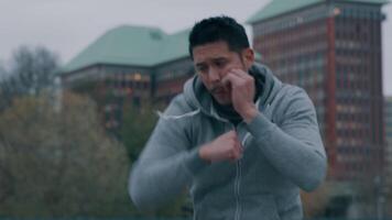 Asian young man in park, doing physical exercise, boxing movements with arms and fists in front of him, turning around video