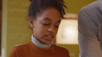 Black girl looks down whilst talking to man next to her. Light of device reflects on her face. Part of face and shoulder of man seen on the right camera video
