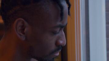 Close up of black man looking through window whilst putting on face mask, adjusting it video