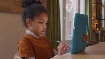 Black girl sits at table. Holds tablet in front of her. Makes lines with stylus pen on screen of device. She talks, turns her head, turns her head to tablet, twice video