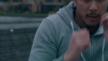 Young Asian man in park, doing physical exercise, by making boxing movements with arms and fists, bends and holds moving hands in front of his face, defending moves. Slow motion, close-up, frontal video