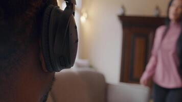 Close up of right part of back of the head of mature man with headphone on ear. Mature woman enters, sits down on couch, talking nervously, moving arms and hands, prominently. Man takes off headphone video