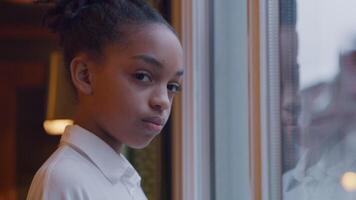 Black girl in front of window, head turned to camera, looking seriously through window and into camera lens video