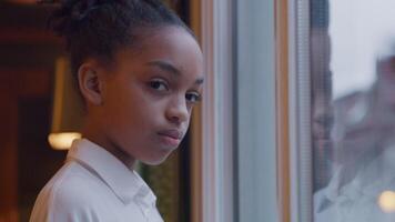 Black girl stands in front of window, head and eyes turned to camera, looking serious video