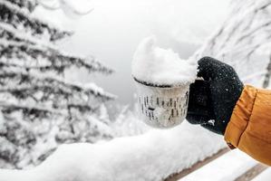 Hand in knitted glove holding mug of snow
