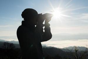 Silhouette of young photographer holding a camera with mountain landscape photo