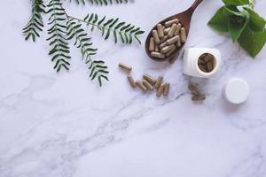 Medicina herbaria en cápsulas en cuchara de madera con hoja verde natural sobre mármol blanco