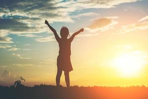 Silhouette of little girl raising hands for freedom photo