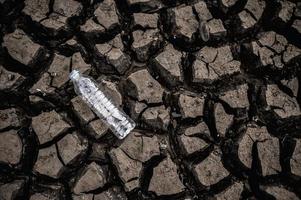 botella de agua en suelo seco con tierra seca foto