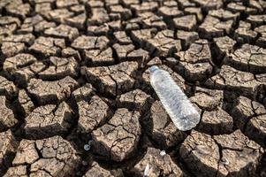 botella de agua en suelo seco con tierra seca foto