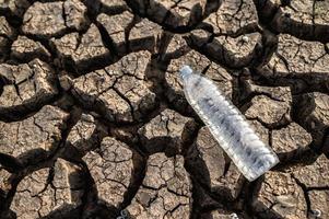 botella de agua en suelo seco con tierra seca foto