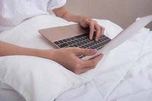 Woman using laptop while sitting on bed photo