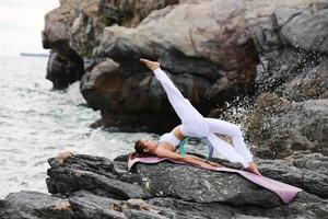 Una mujer delgada y saludable practicando yoga en una roca en una costa foto