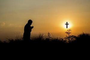 Silhouette of man praying in front of cross with faith and belief photo