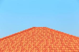 Orange tiles on a roof of a house against a blue sky background photo