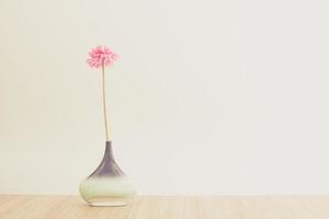 Still life of a pink flower in a vase on the top of a wooden table