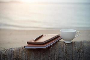 cuadernos, un bolígrafo y una taza de café en la playa foto