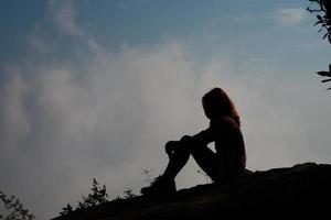 Silhouette of a hiker sitting on mountain top with blue sky background photo