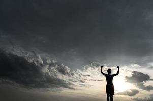 Silhouette of a boy raising his hands in the sky photo