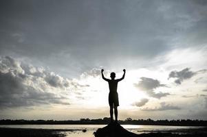 Silhouette of a boy raising his hands in the sky photo