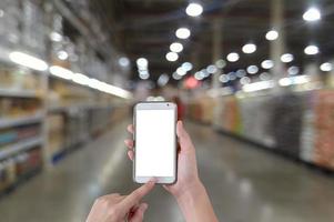 Manos con teléfono inteligente móvil de pantalla en blanco con fondo borroso en el supermercado foto