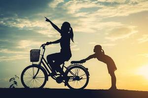 Silhouette of mother with her daughter on a bicycle photo