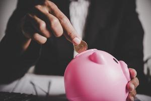 Person putting coins into a piggy bank on the table photo