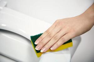 Mujer joven limpiando un asiento de inodoro con una esponja foto