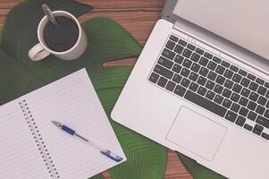 Laptop, notebook, pen, coffee and a palm leaf on a wooden table photo