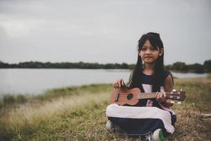 Cute little asian girl sitting on grass and playing ukulele in the park photo