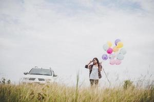 Beautiful young hipster woman holding colorful balloons outdoors photo