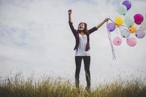 Beautiful young hipster woman holding colorful balloons outdoors photo
