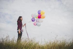 Beautiful young hipster woman holding colorful balloons outdoors photo