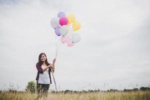 Beautiful young hipster woman holding colorful balloons outdoors photo